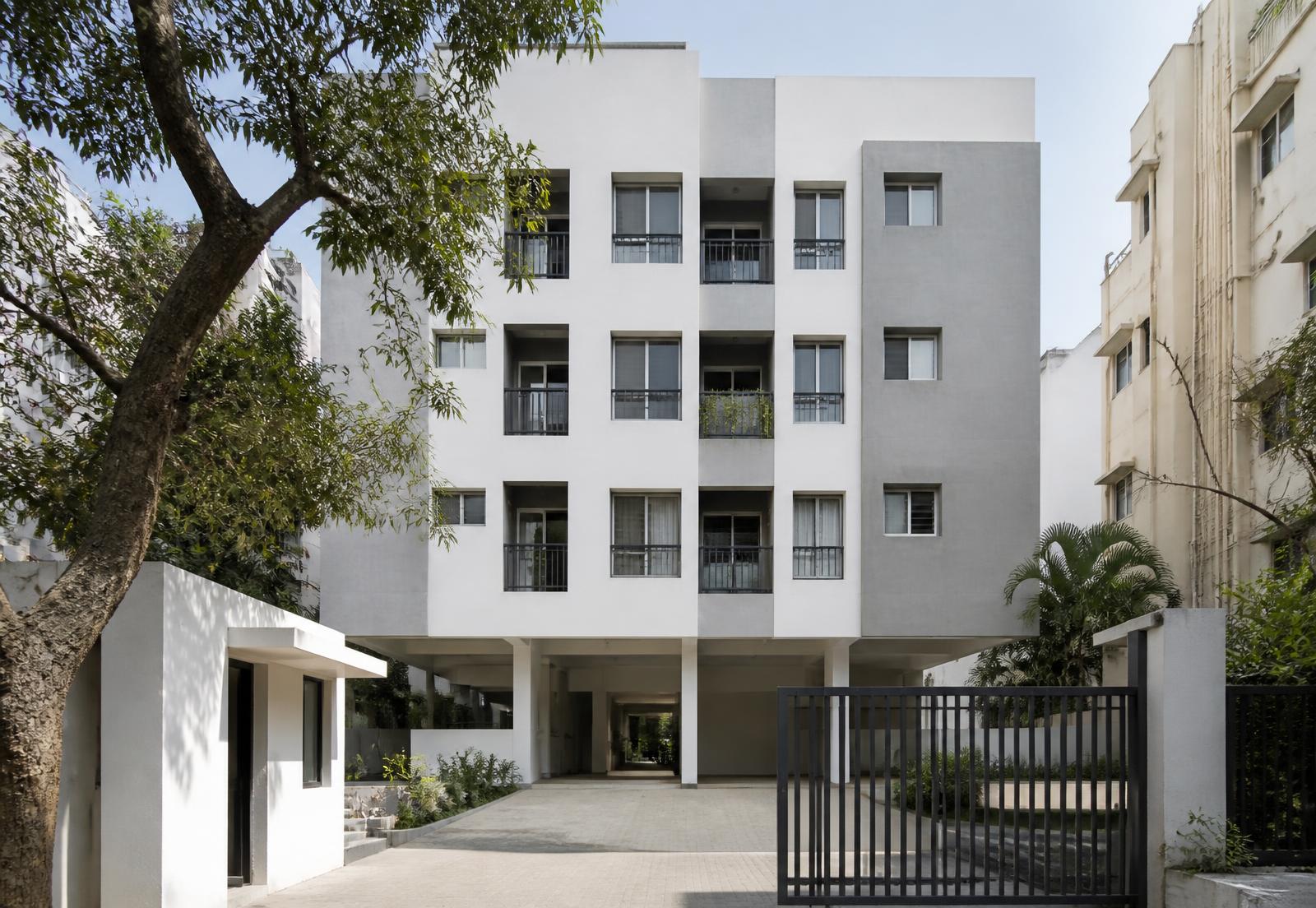 Clean white and grey four-storey apartment building with slim balcony railings and a stilt parking entrance